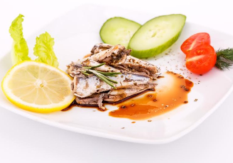 Fish, vegetables and lemon on white plate.